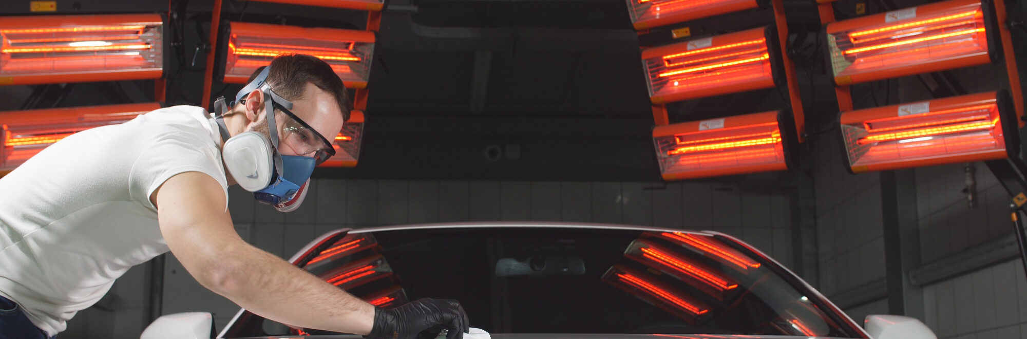 man in glasses and a mask, a respirator polishes the car with a sponge and a special chemical composition to protect the paint on the body from scratches.