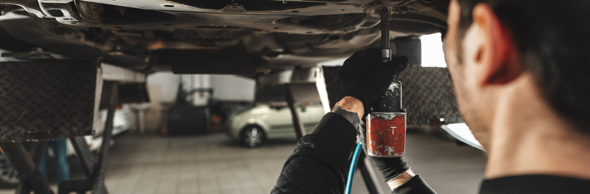 Workman mechanic working under car in auto repair shop close up